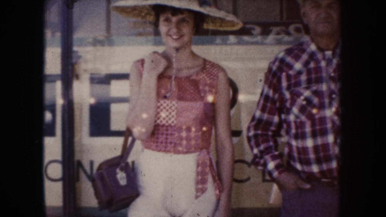Woman in a wide straw hat smiles while holding a handbag beside a man in plaid.