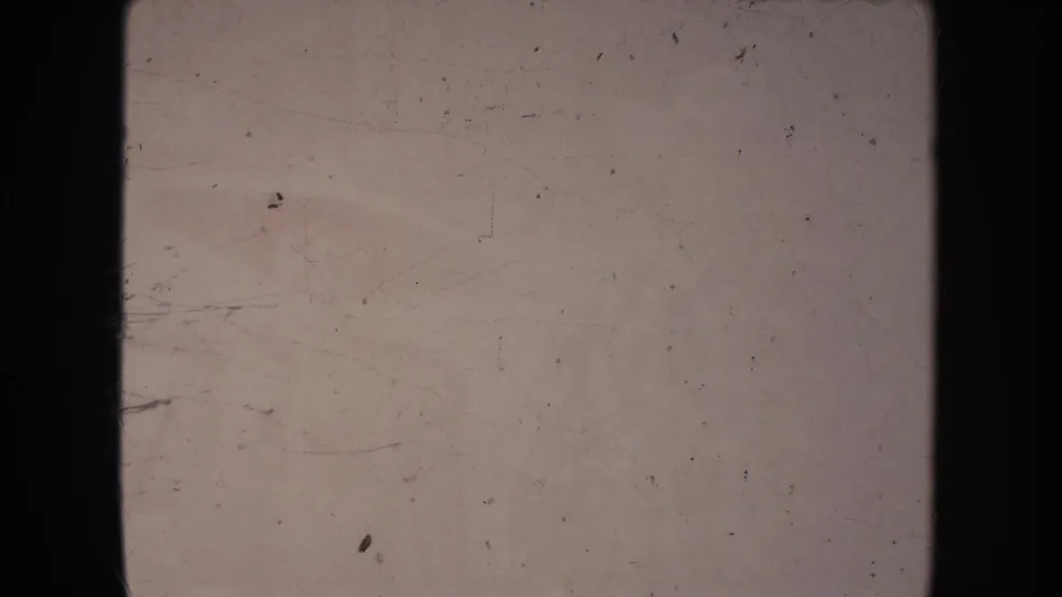 A heavily worn 8mm frame from the clip shows pale exposure, dust, scratches, and dark film borders with no clear subject visible.