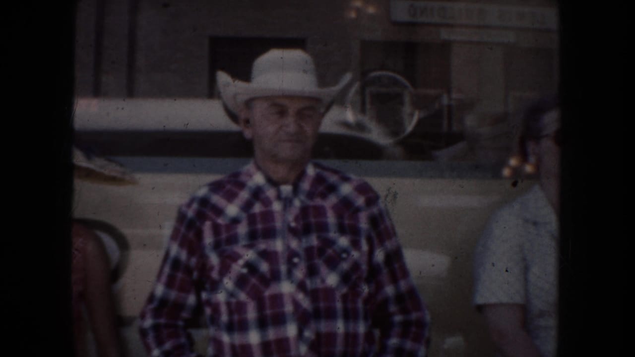 In 1954 South Dakota footage, a man in a white cowboy hat and plaid shirt stands beside a parked car with another person partly visible.