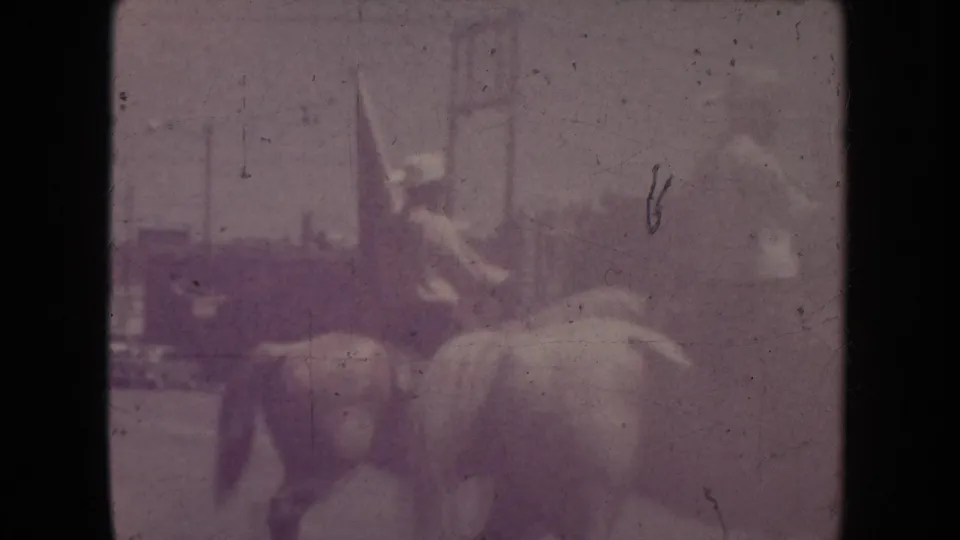 A faded 1954 South Dakota parade frame shows a horse and rider with a flag, softened by exposure and film wear.