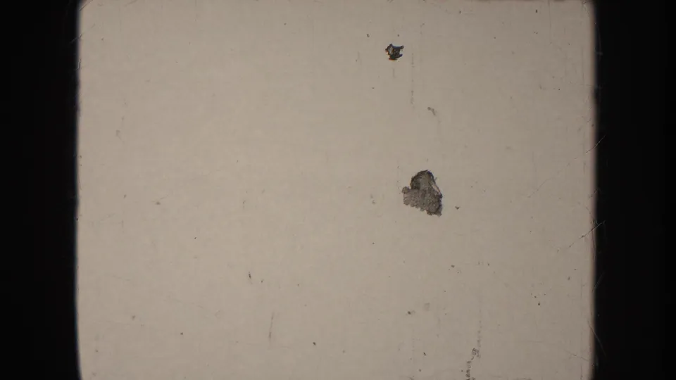 A pale 8mm frame with dark borders, visible dust, scratches, and small marks before the parade action begins.