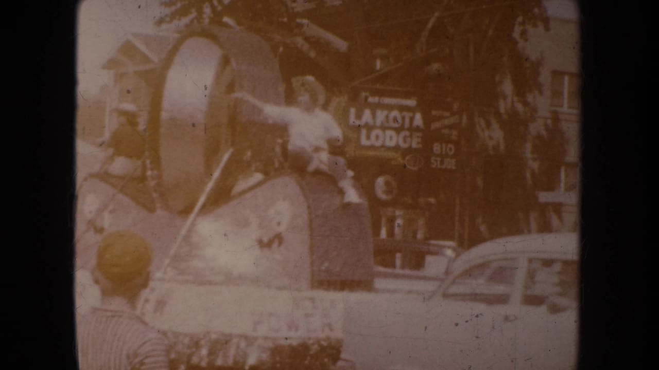 1954 South Dakota parade footage appears to show a decorated float or figure near a Lakota Lodge sign with a child at the lower left.