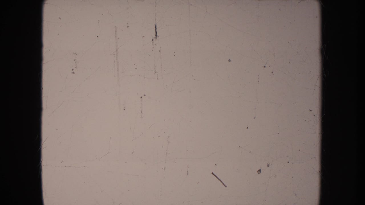 Pale South Dakota home-movie frame with 8mm borders, scratches, and no clearly identifiable parade detail in this still.