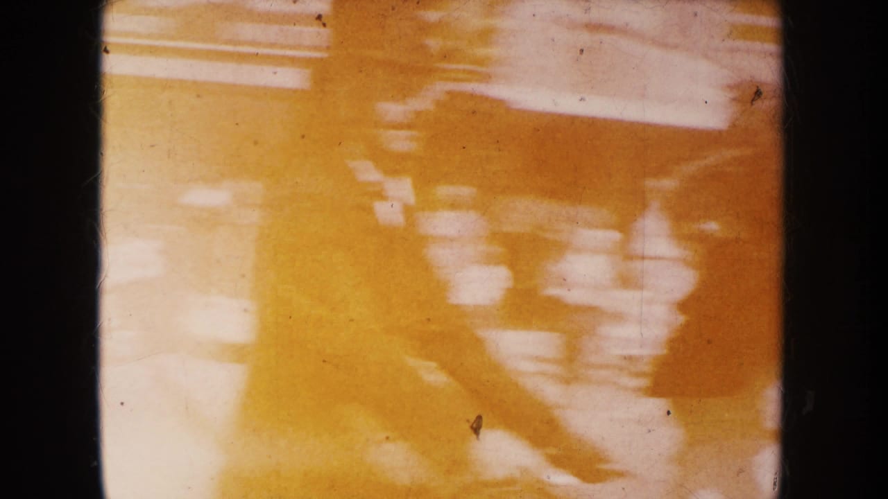 Amber 1950s South Dakota home-movie frame with blurred parade-like motion, light shapes, scratches, and heavy color fading.