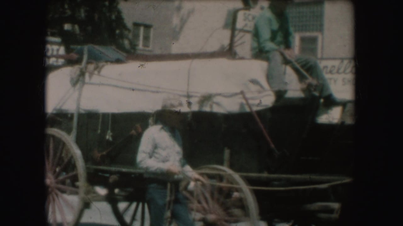 1954 South Dakota street frame with carriage wheel, horse body, seated person, and downtown storefront signage in view.