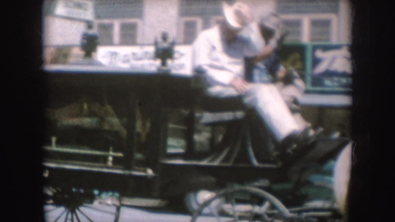 1954 South Dakota home-movie frame showing a cowboy-hatted rider on the front bench of a horse-drawn carriage in town.