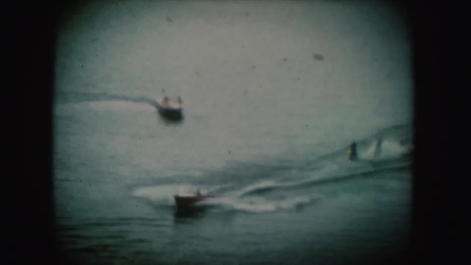1954 South Dakota home-movie frame showing small boats moving across water, with wakes visible on the surface.