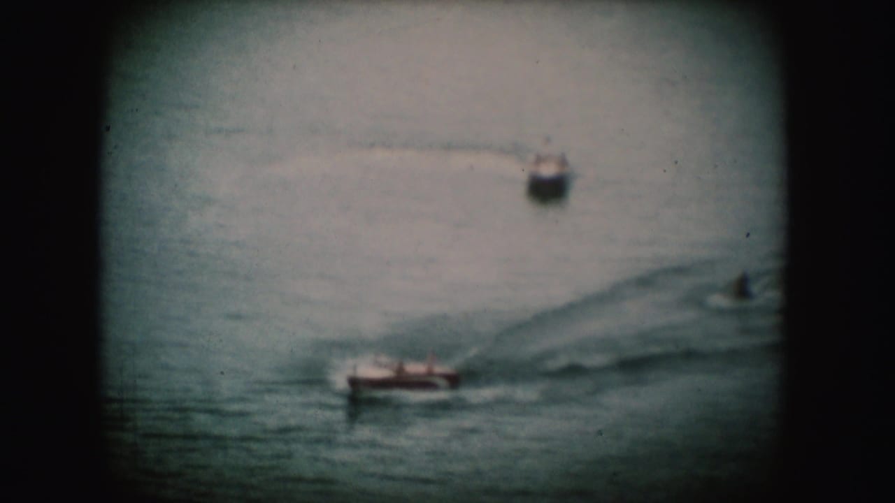 A red-toned boat crosses the lower water while another boat travels farther back.