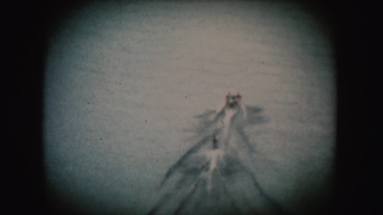 1954 South Dakota 8mm frame showing a distant tow boat, wake, and small water-skier form on a river.