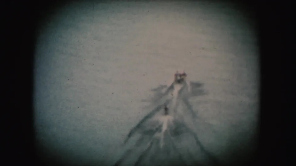 1954 South Dakota 8mm frame showing a distant tow boat, wake, and small water-skier form on a river.