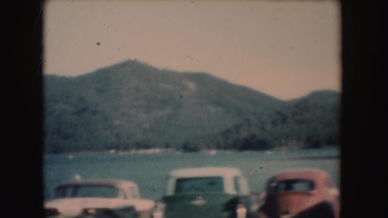 1954 South Dakota home-movie frame showing multiple parked cars along a mountain lake shore.