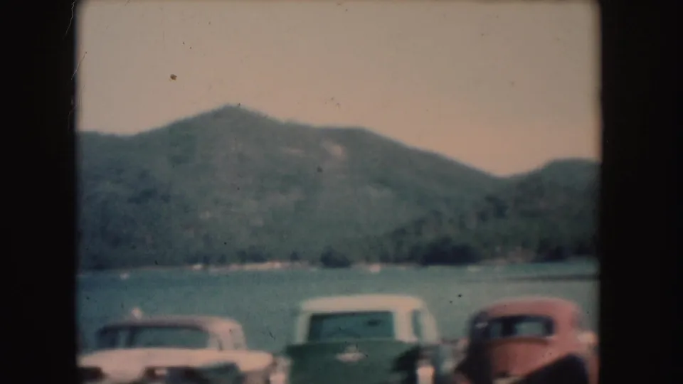 1954 South Dakota home-movie frame showing multiple parked cars along a mountain lake shore.