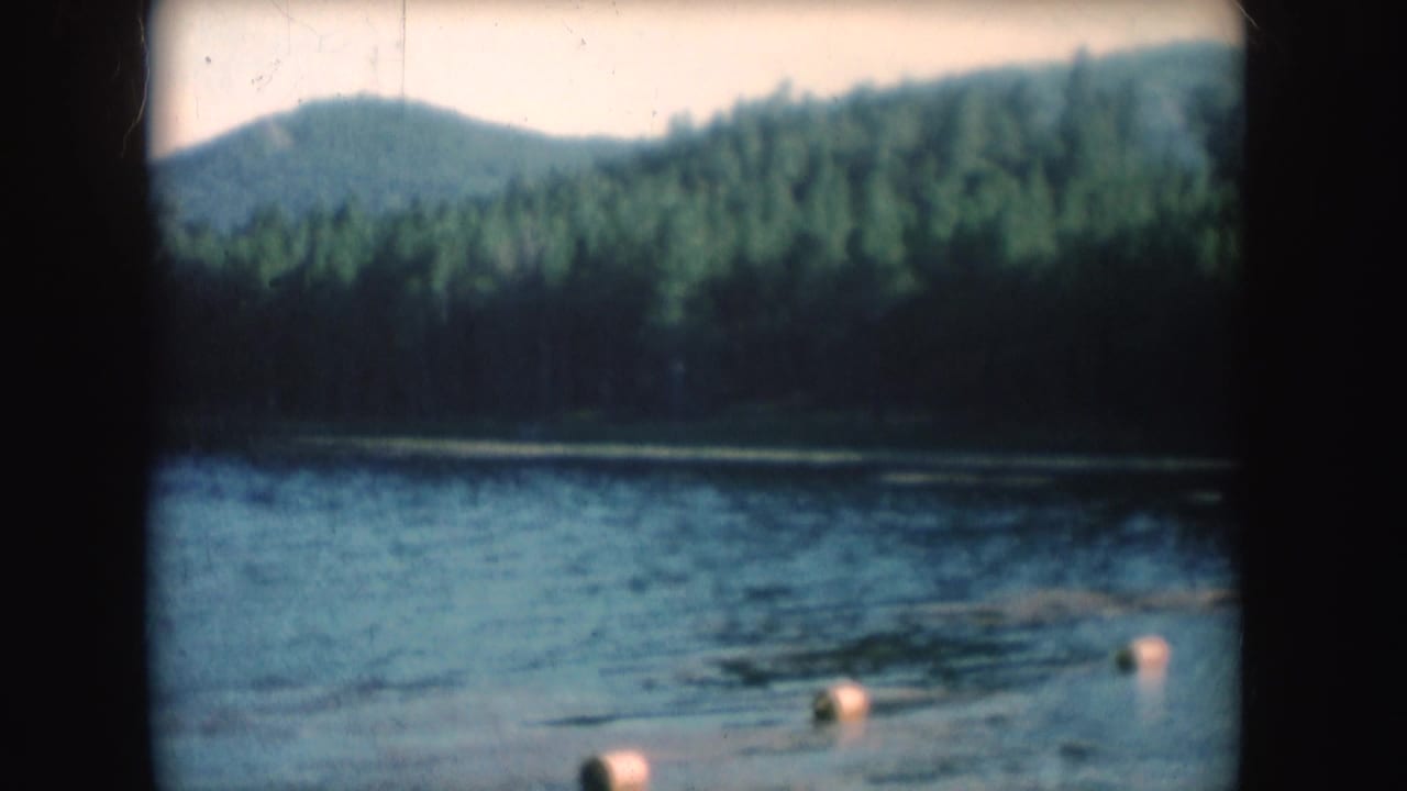 Calm lake with forested shoreline and hills beyond, seen through dark 8mm frame edges.