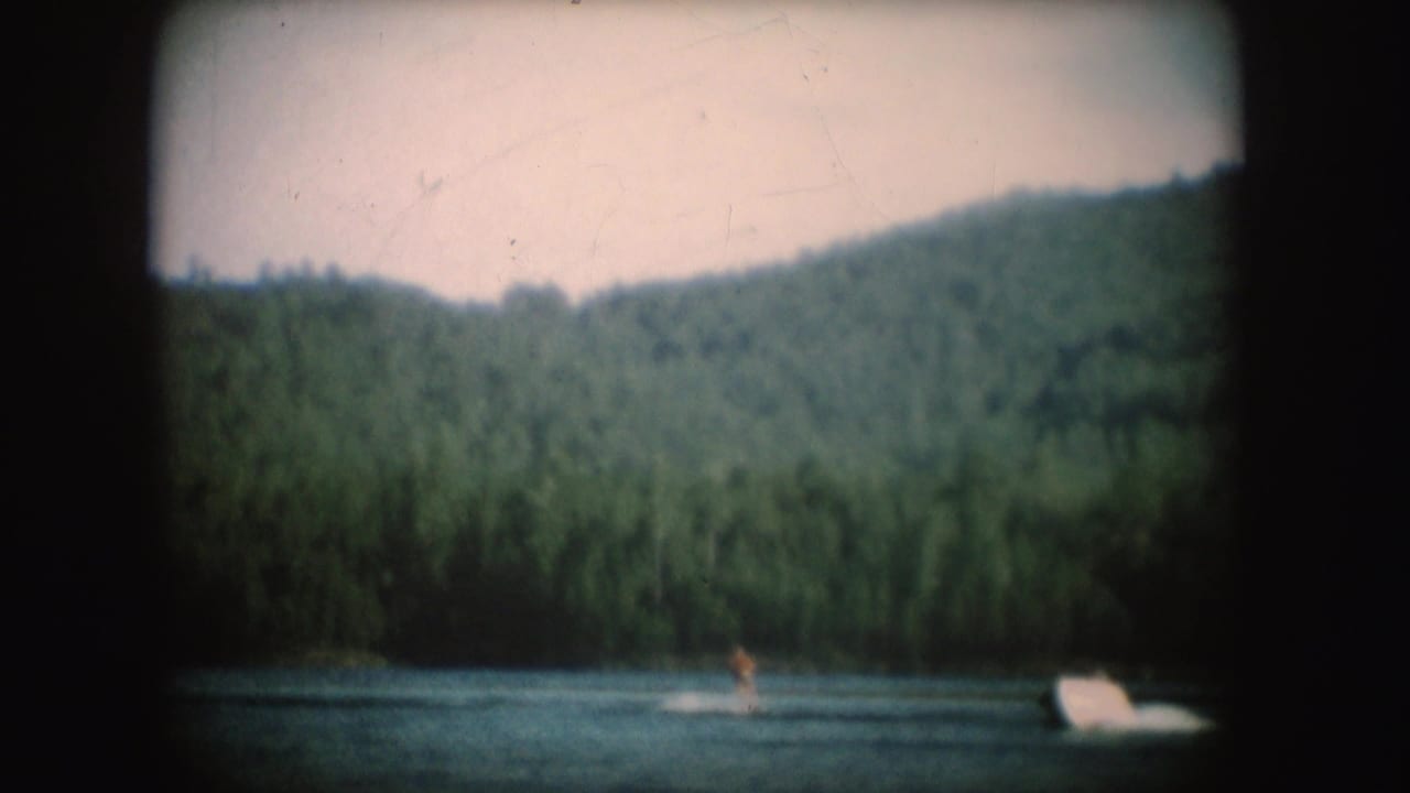 A motorboat and distant water skier cross a South Dakota lake with wooded hills behind them in 1954 8mm footage.