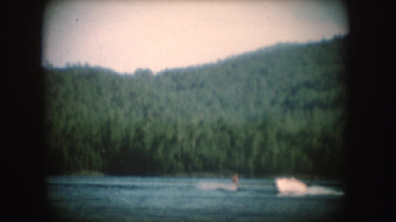 Water skier and motorboat moving across a forested lake.