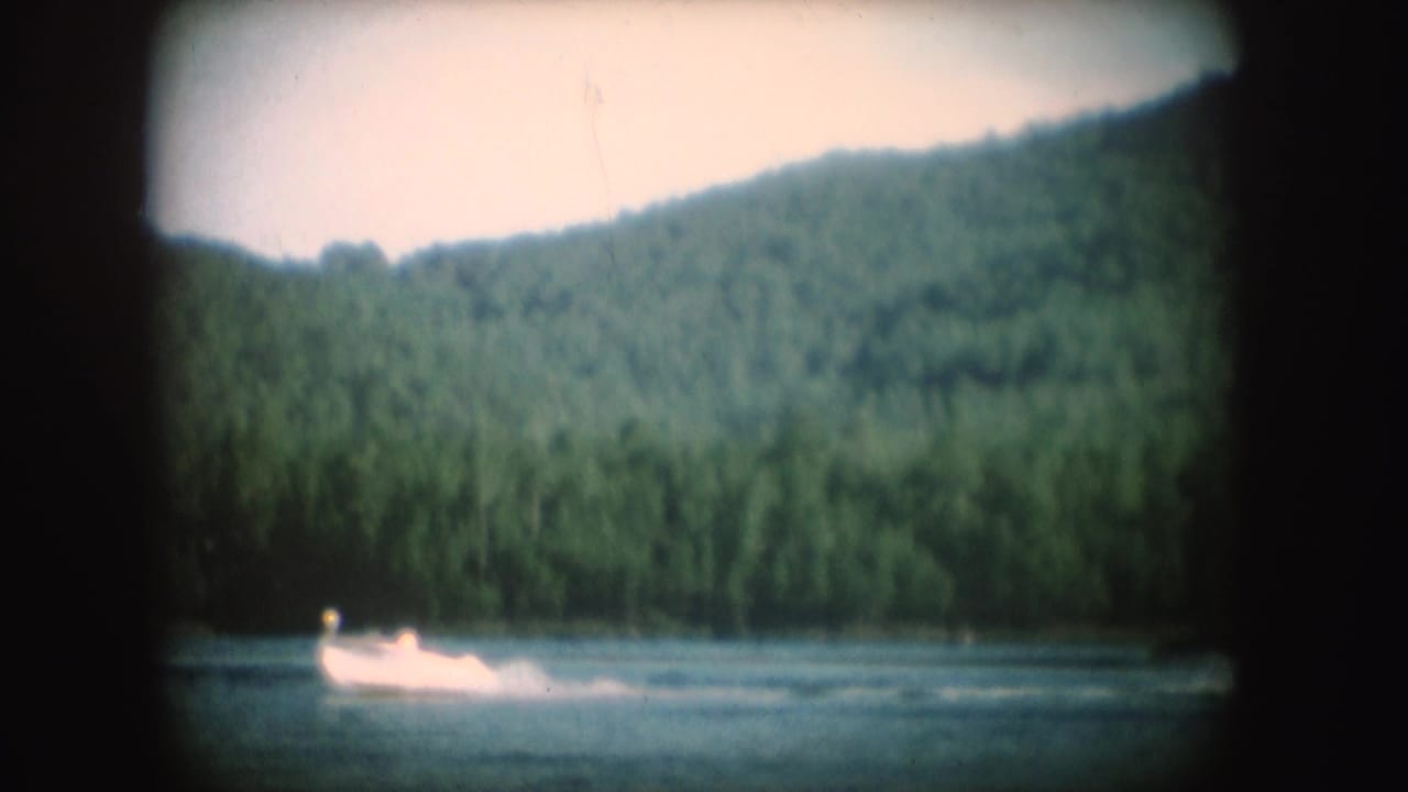 Soft 8mm South Dakota lake frame with the motorboat and wake low in the scene against dense green hillside.
