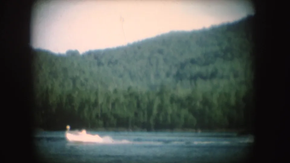Soft 8mm South Dakota lake frame with the motorboat and wake low in the scene against dense green hillside.