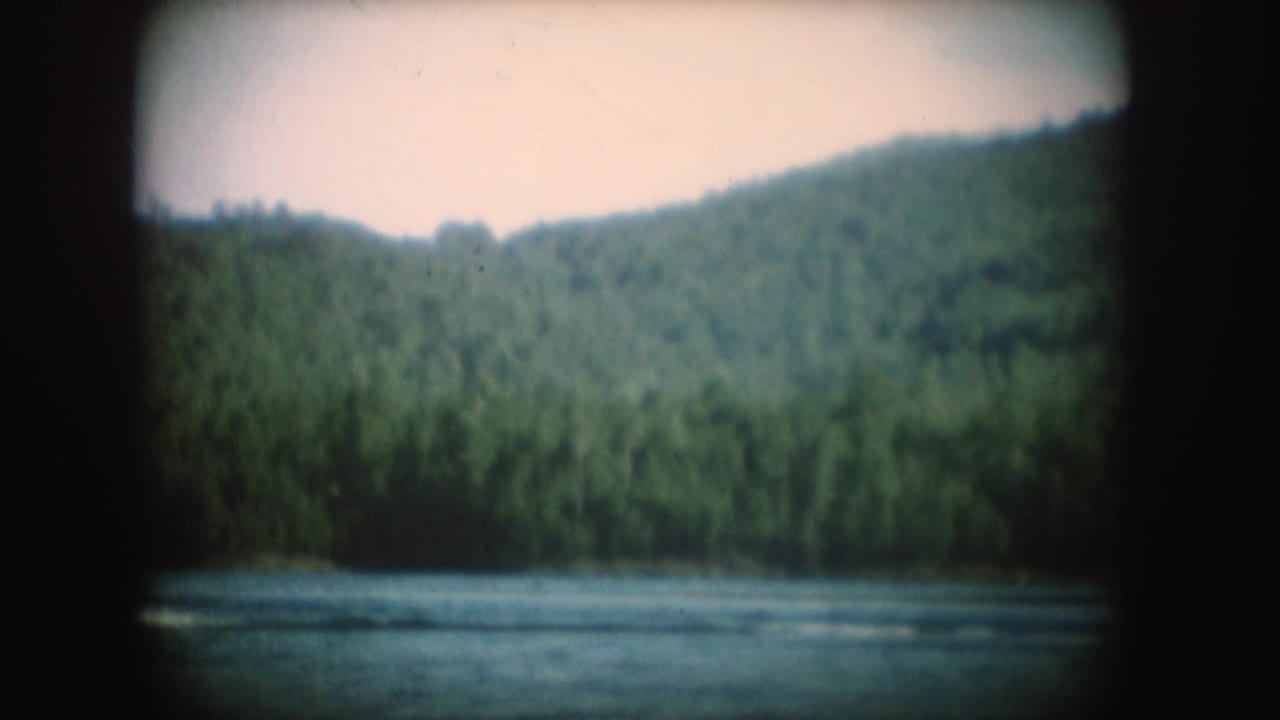 1954 South Dakota 8mm frame showing a calm lake below wooded hills, with no clear person visible in this moment.