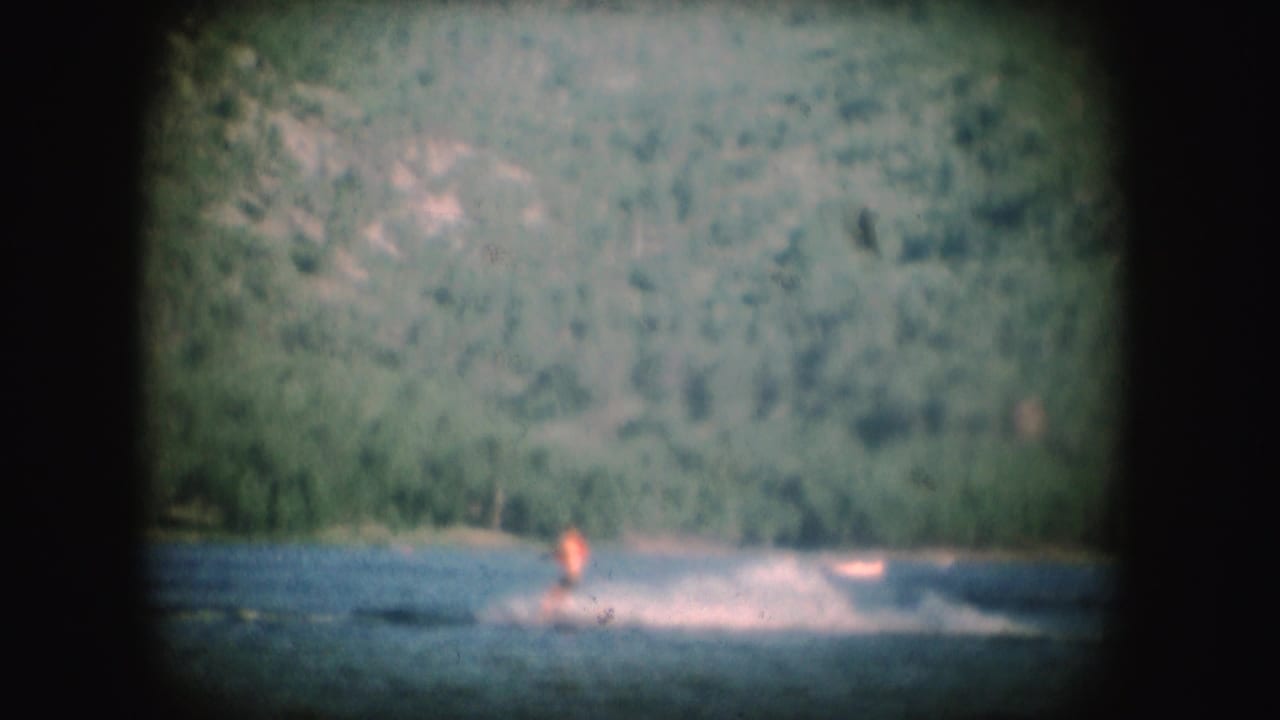 A distant water skier in an orange top rides through lake spray in this soft 1954 South Dakota 8mm frame.