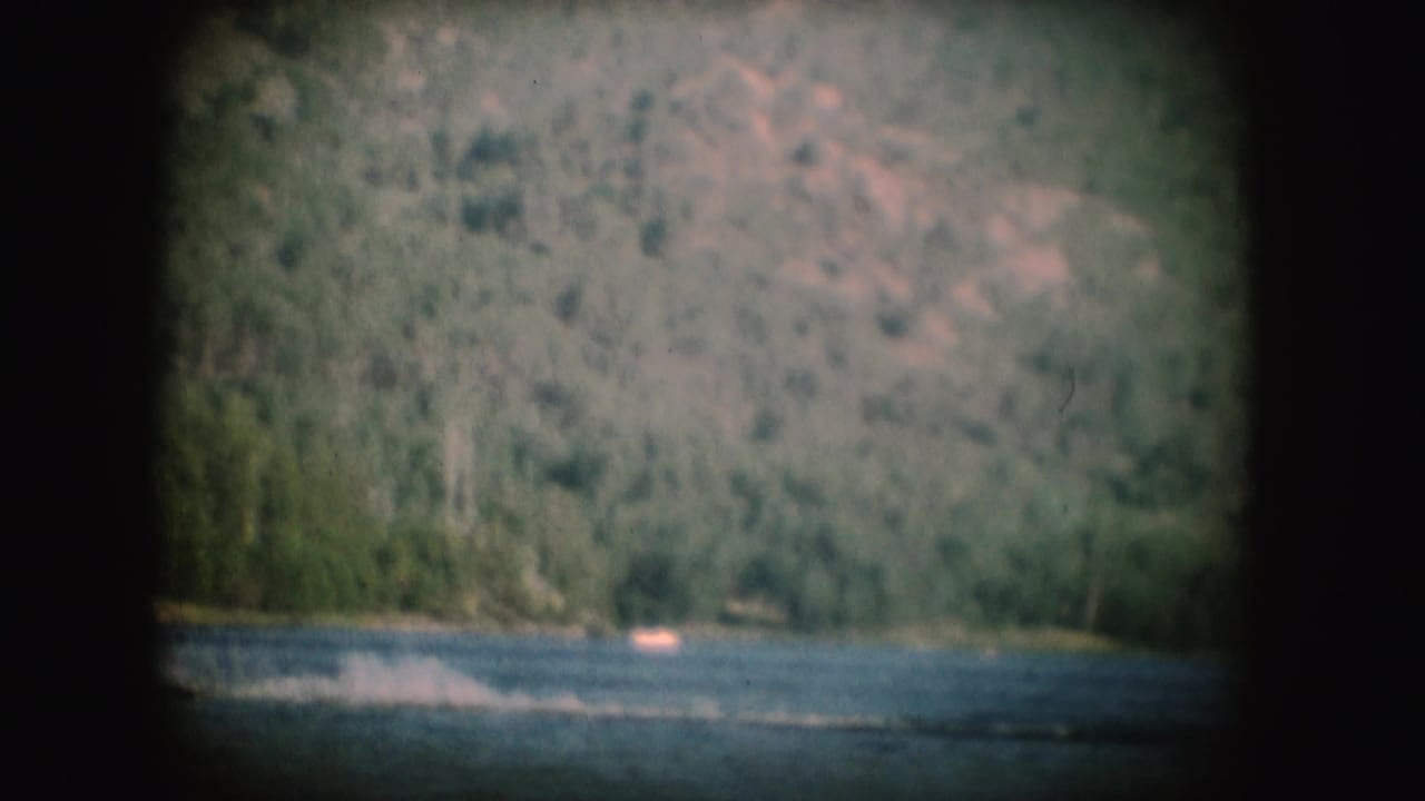 The final frame shows the lake surface, faint water-skiing spray, and a small boat below wooded South Dakota hills.