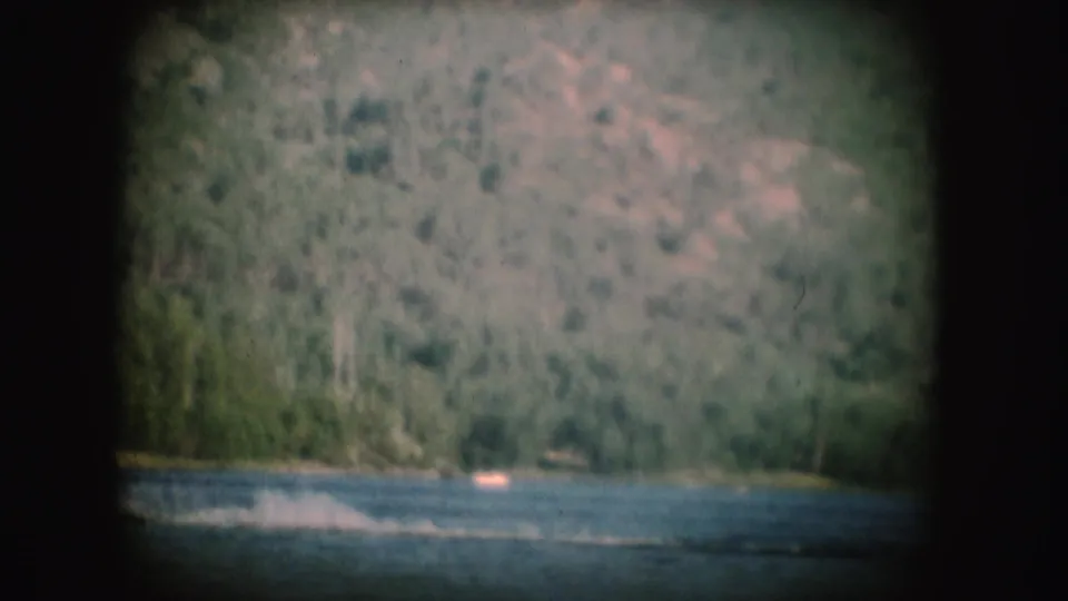 The final frame shows the lake surface, faint water-skiing spray, and a small boat below wooded South Dakota hills.