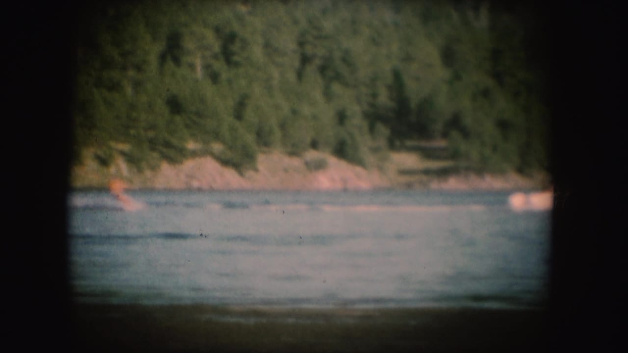 Soft 8mm South Dakota lake frame with a small distant water skier near the left and a wooded shore behind.