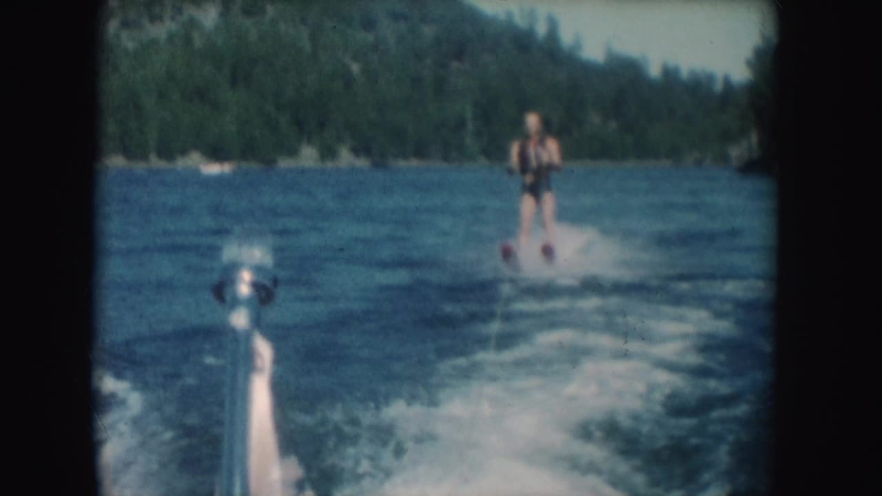 A man water skis behind a moving speedboat on a South Dakota lake, with wake spray and boat hardware visible in the 8mm frame.