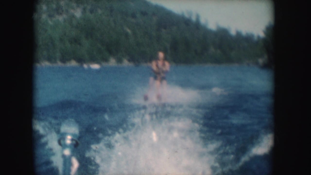 Soft 8mm frame of a man water skiing through a broad wake on a forested South Dakota lake in 1954.