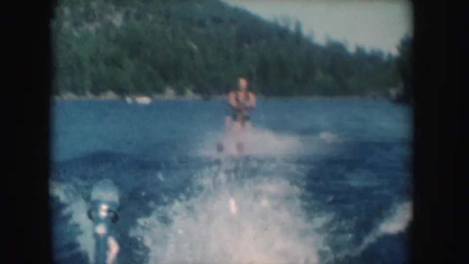 Soft 8mm frame of a man water skiing through a broad wake on a forested South Dakota lake in 1954.