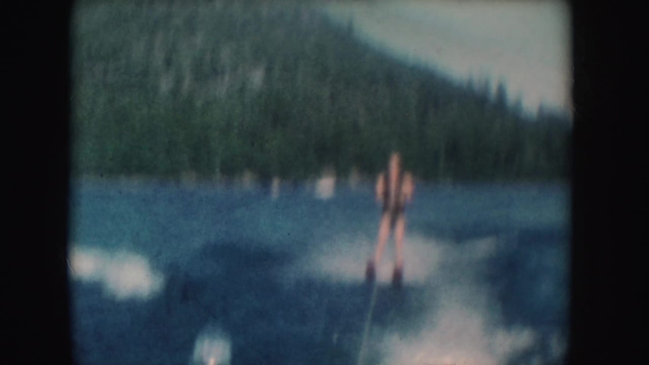 Distant view of a male water skier on a mountain lake, with tow rope, wake, and green South Dakota hills visible.