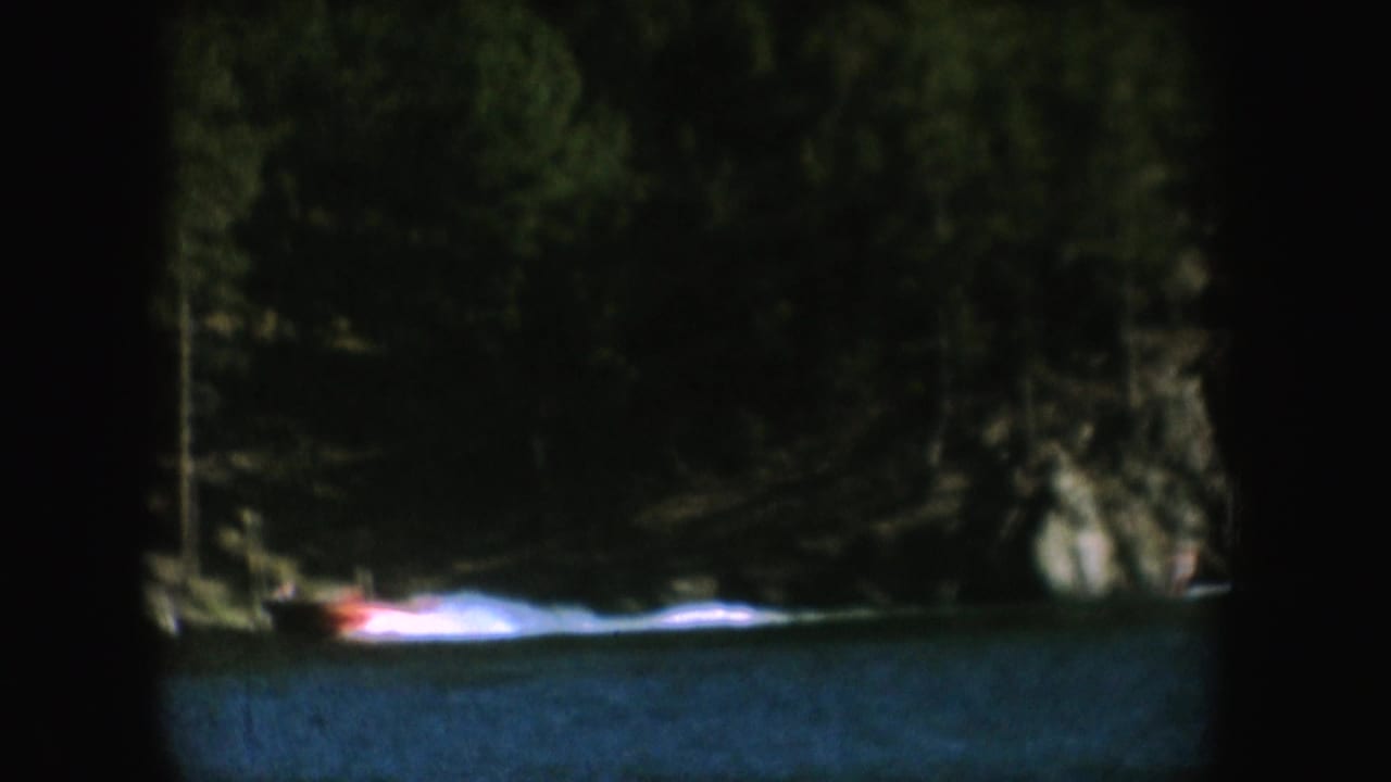 Small motorboat moving across a dark blue lake near a forested shoreline.