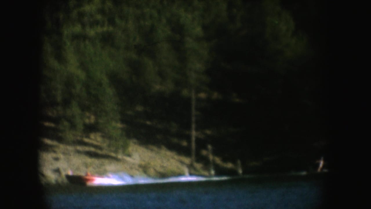 A motorboat moves beside a wooded shoreline on a South Dakota lake, filmed on color 8mm with muted exposure.