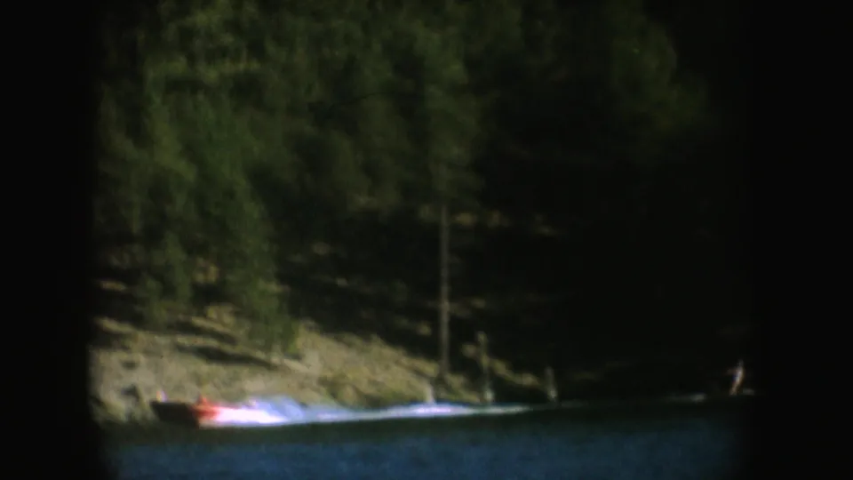 A motorboat moves beside a wooded shoreline on a South Dakota lake, filmed on color 8mm with muted exposure.