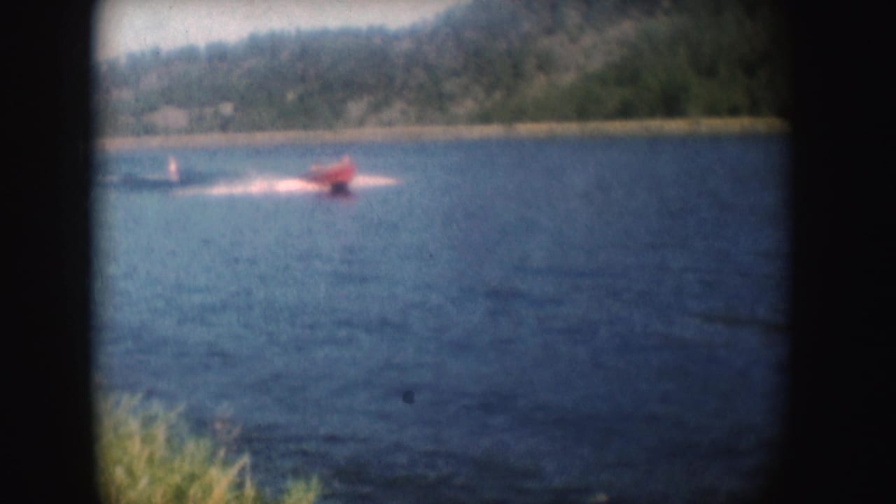 Red speedboat on South Dakota water in 1954, seen from shore with trees and hillside beyond.