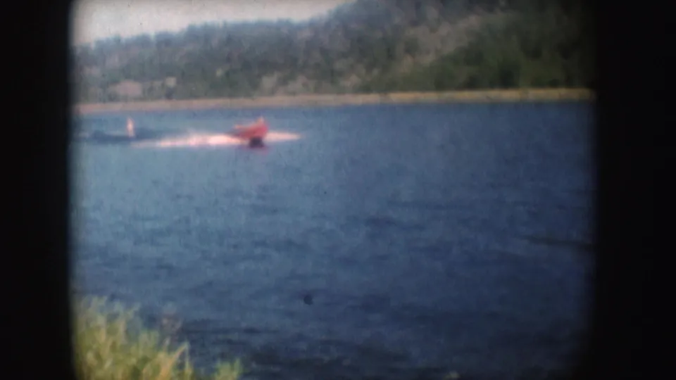 Red speedboat on South Dakota water in 1954, seen from shore with trees and hillside beyond.