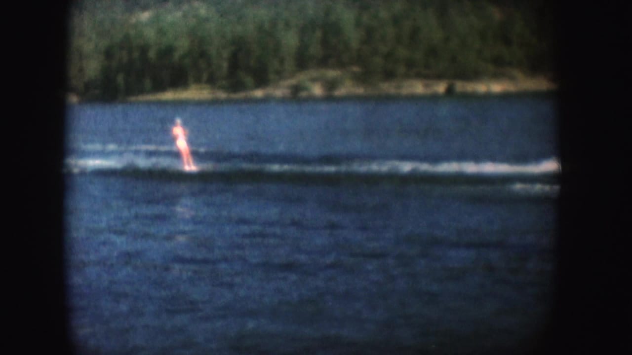 Distant water skier upright on a lake near a long wake.