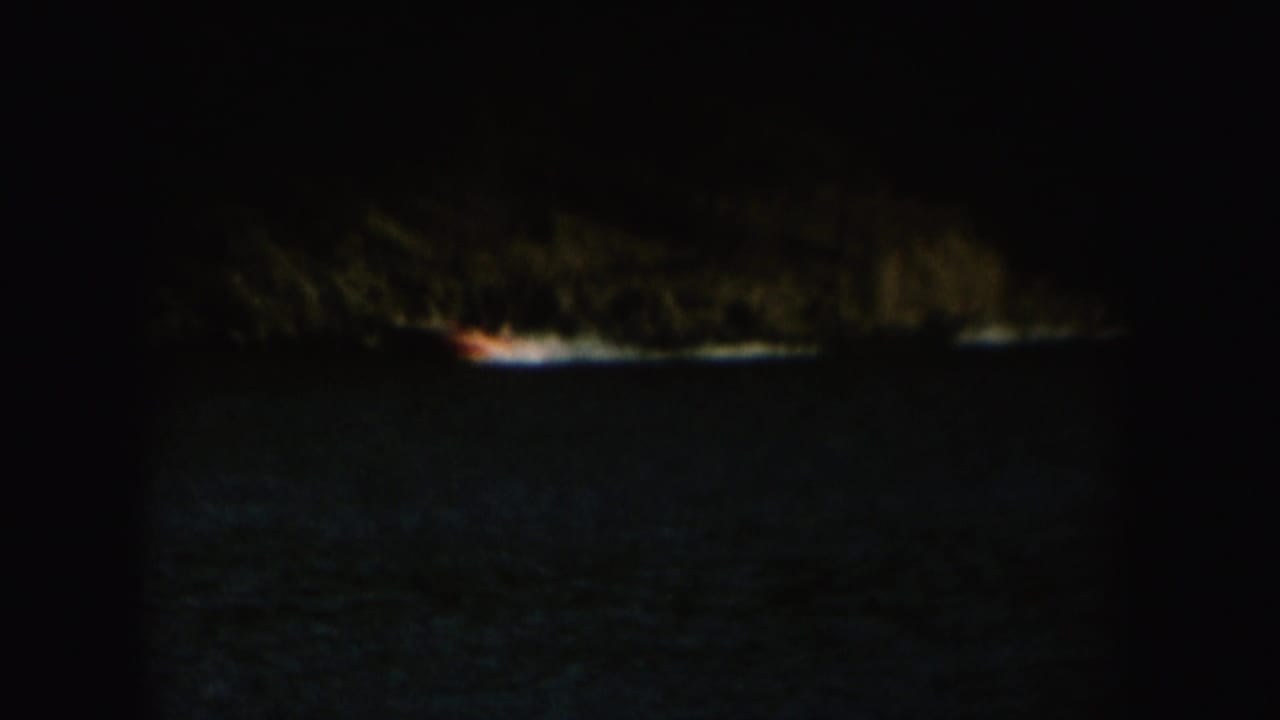 Distant boat towing a water skier across dark lake water near a wooded shore.