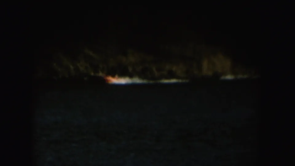 1954 South Dakota 8mm frame showing a small boat and water skier moving across a lake below a dark shoreline.