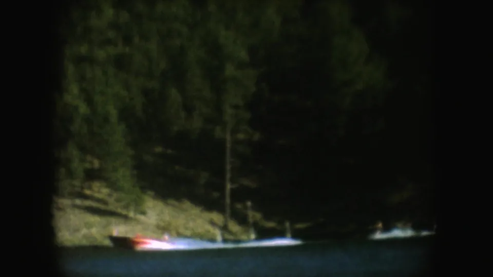 A small boat appears low in frame beside a wooded South Dakota lakeshore, filmed in soft 8mm color.