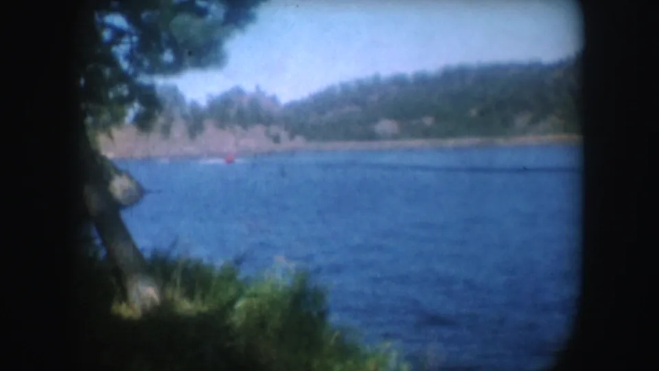 Bright South Dakota lake view with blue water, distant wooded hills, and shoreline seen through rounded 8mm frame edges.
