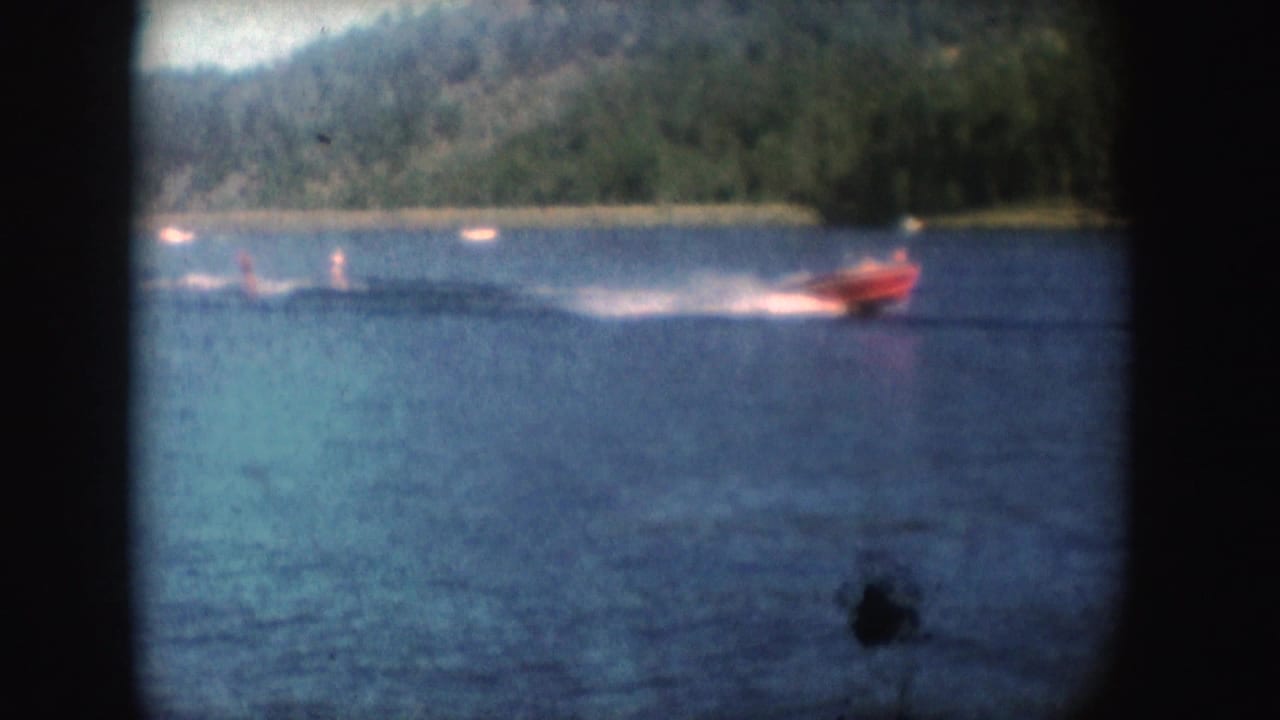 A red motorboat appears to tow water-skiers across a lake in 1954 South Dakota home-movie footage.