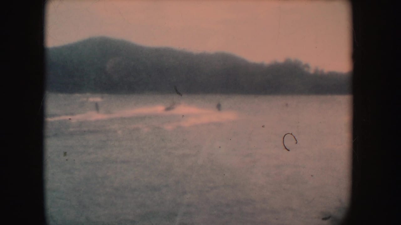 Distant motorboat crossing a lake near wooded hills with a pale sunset tint.