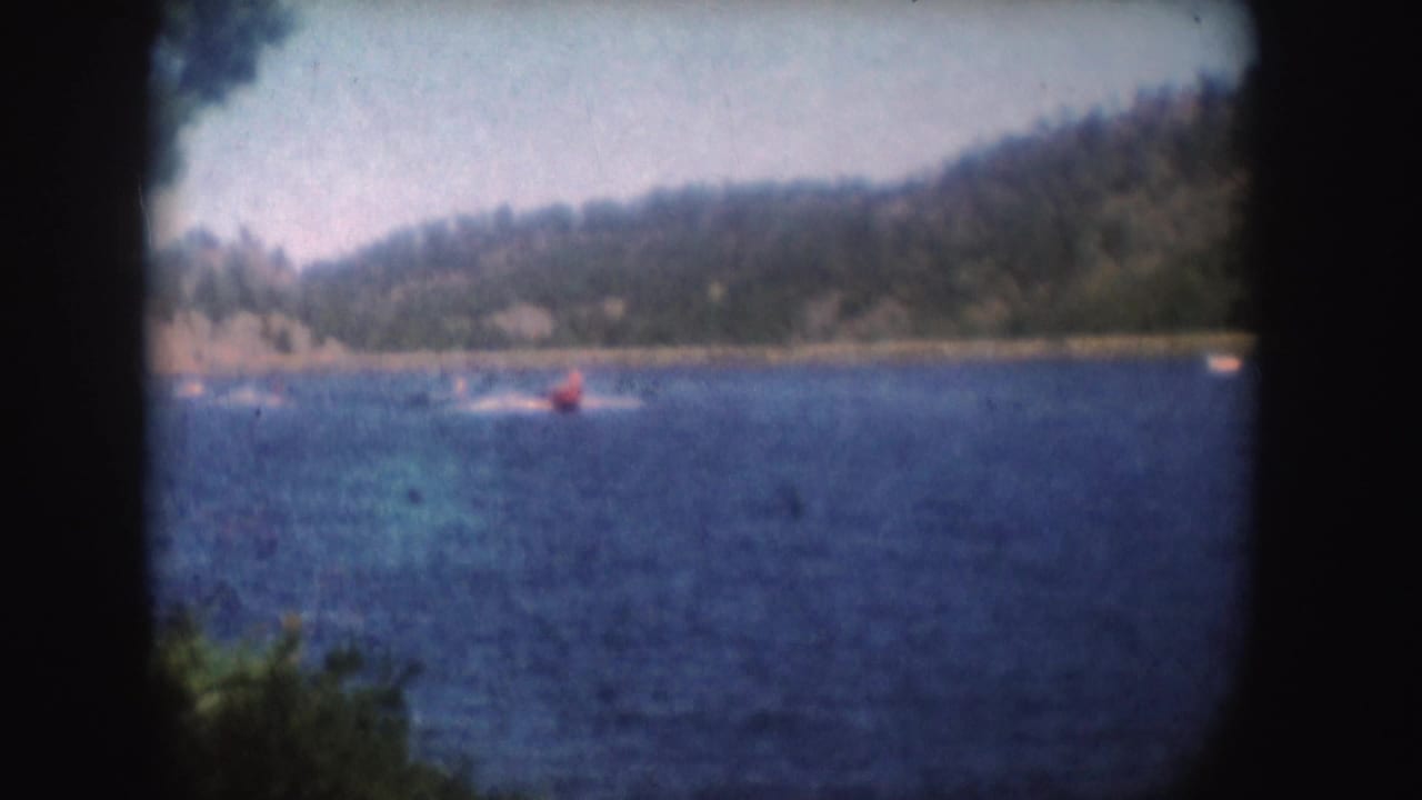 Red speedboat moves across open lake water with hills behind it.