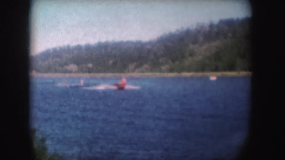 A red speedboat crosses a South Dakota lake in 1954 home-movie footage, with wooded hills in the background.