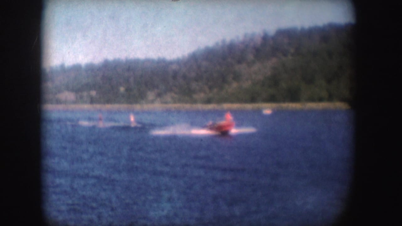 Red speedboat moves across the lake while two water skiers trail behind in its wake.