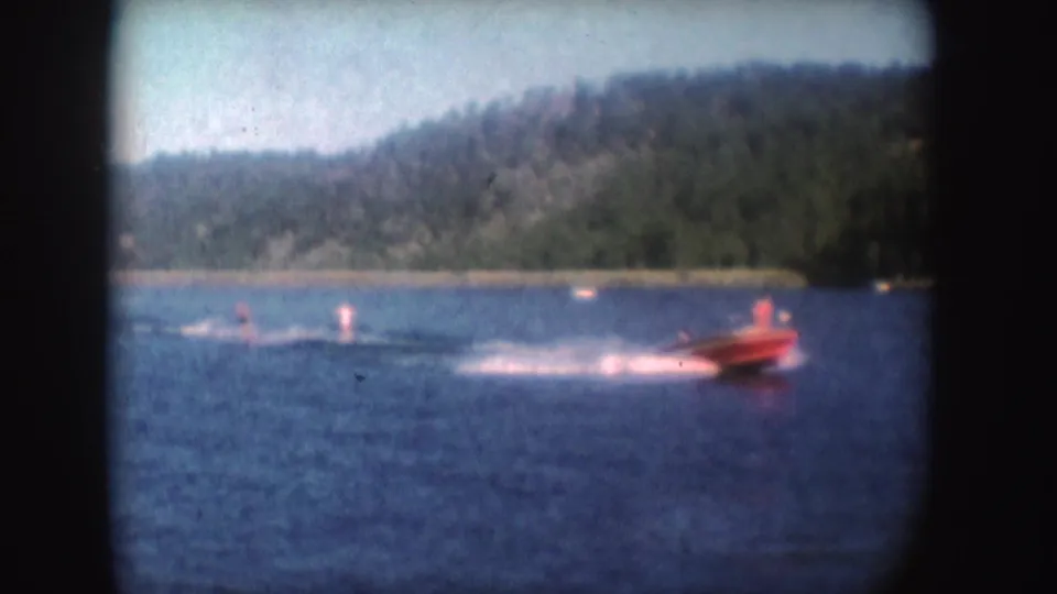 Soft 8mm frame from 1954 showing a red speedboat and two water skiers on a South Dakota lake.