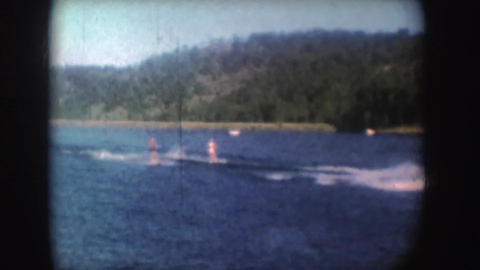 Distant water skiers ride through the wake on a South Dakota lake, with the towing boat partly out of view.