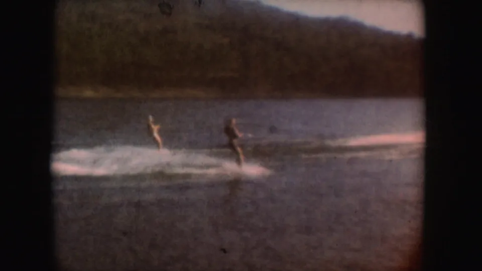 Two men water ski across a South Dakota lake in a soft, faded 1954 8mm home-movie frame.