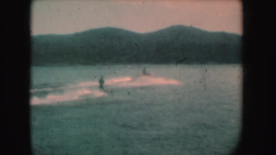 Distant water skiers on a South Dakota lake, with low hills and soft color fading in the 1954 8mm frame.