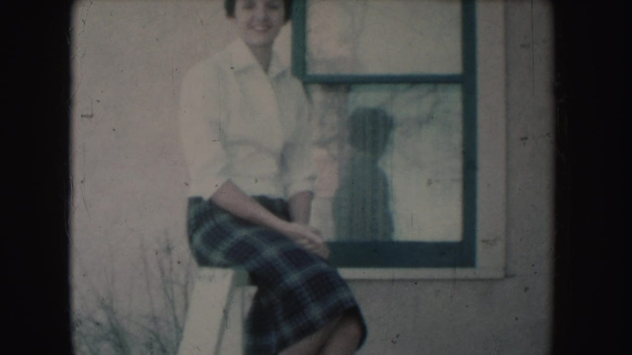 Seated young woman smiles near a window, with her shadow visible on the glass.